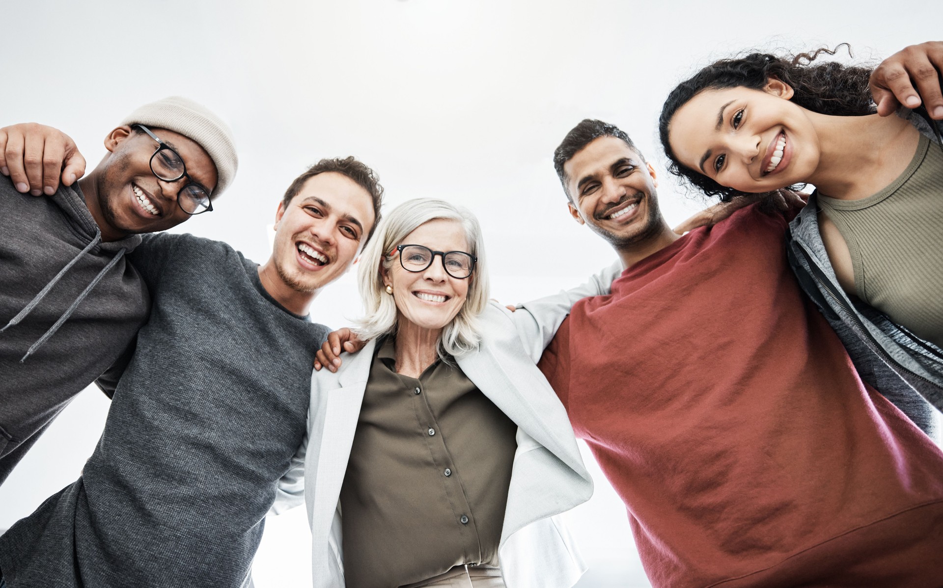 Low angle portrait of team of business people hugging each other. Diverse group of men and women standing in a together in their office, huddling and smiling. Unity and teamwork is key to success